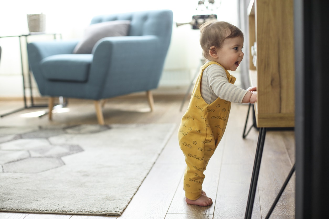 Little girl takes her first steps alone and is supported by the furniture in the living room