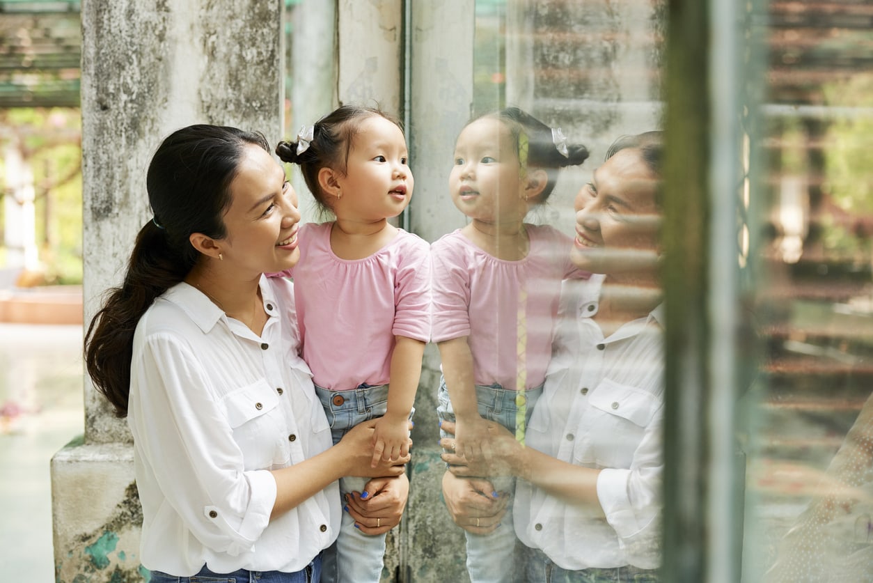 Mother and her curious daughter stand at the glass window in the zoo and look at animals