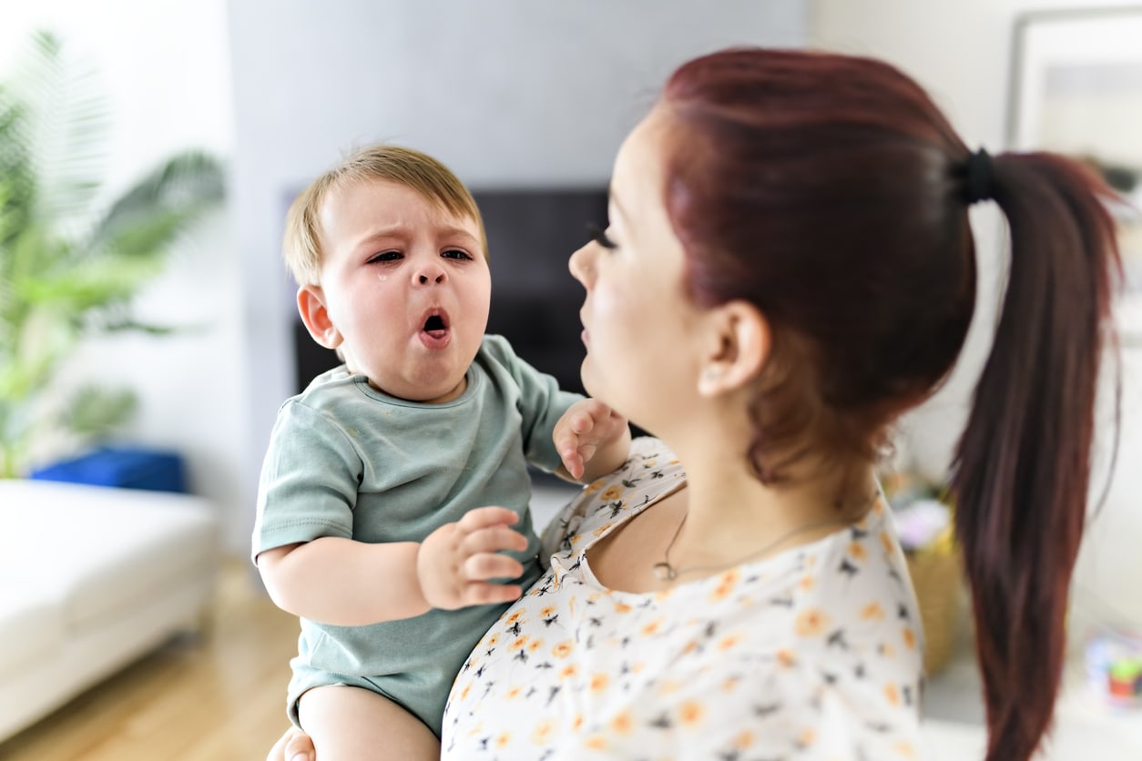 A mother holds her child in the living room. The baby is sick and has a cough